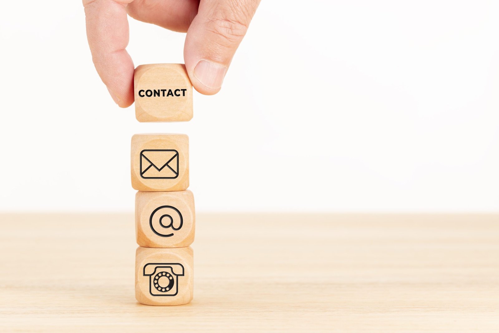 Contact us concept. Hand holding a wooden block with text and a pile of dices with communication icon. Copy space